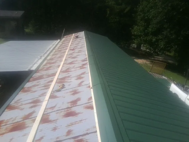 Old rusted panels beside newly installed green metal roofing — Wind Damage Roof Repair by Roofing Brothers in Groton