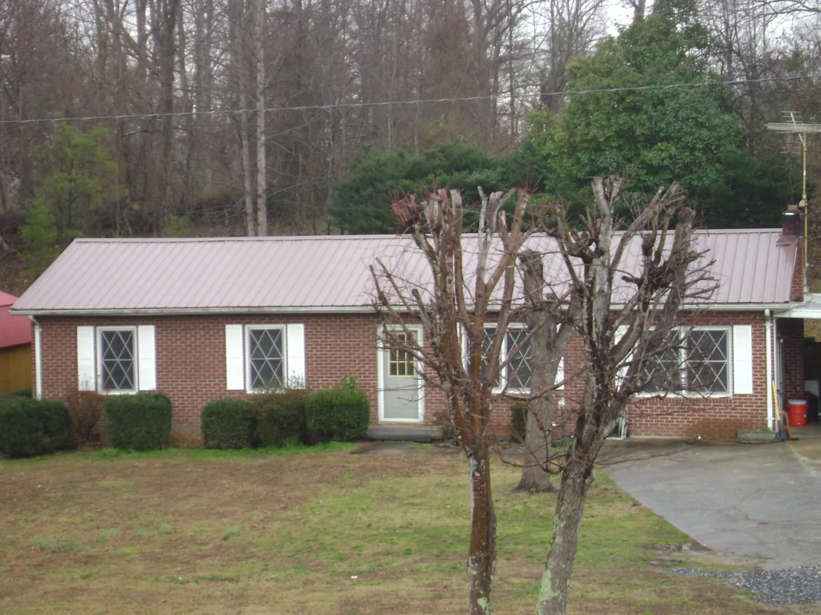 Mauve metal roof on a brick ranch home behind bare trees in Groton