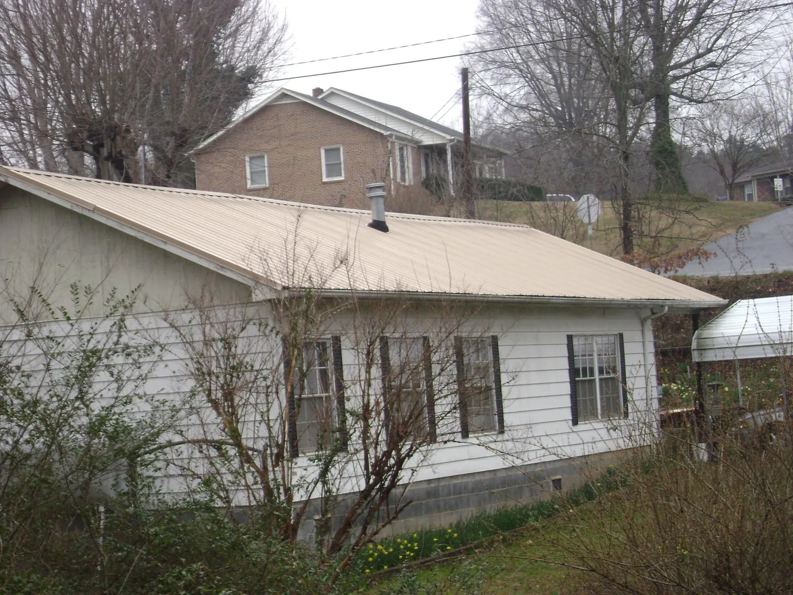 Tan metal roof on a white sided house set into a hillside — Commercial Roofing by Roofing Brothers in Groton